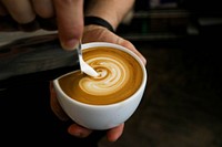 A person's hands holding a coffee cup and pouring cream into it. Original public domain image from Wikimedia Commons