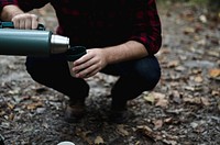 A man in plaid kneeling down and pouring drink from thermos into cap. Original public domain image from Wikimedia Commons