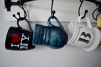 Three mugs on a rack. Two say "I heart NY" and "B." One is plain blue.. Original public domain image from Wikimedia Commons