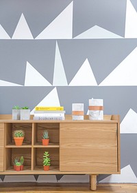 A desk with potted green plants and a stack of books near a wall with a geometric pattern. Original public domain image from Wikimedia Commons