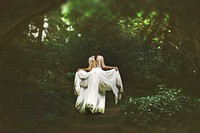 A woman lifting up the ends of her white wedding dress on a forest path. Original public domain image from Wikimedia Commons