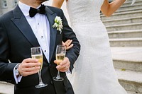 A groom holding two champagne glasses next to a bride in her wedding dress. Original public domain image from Wikimedia Commons