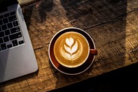 Latte art with a tulip pattern in a cup next to a laptop. Original public domain image from Wikimedia Commons