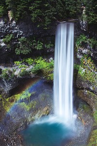 A massive waterfall flowing into a bright blue colored area with a rainbow in British Columbia. Original public domain image from Wikimedia Commons