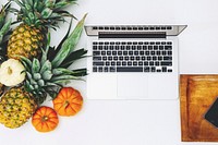 Top view of pineapples and miniature pumpkins and a Macbook.. Original public domain image from Wikimedia Commons