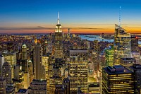 New York City skyline with skyscrapers lit up while sun sets. Original public domain image from Wikimedia Commons