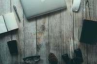 An unplugged typewriter on an office woodwork table holding a pinecone, glass and a writer’s book. Original public domain image from Wikimedia Commons