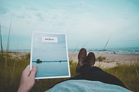 Person lying on the grass at the sand beach holding a magazine Journal. Original public domain image from Wikimedia Commons