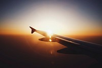 Silhouette of an airplane wing in flight, against the sun setting, with lens flare and vignette effects. Original public domain image from Wikimedia Commons