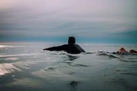 A male surfer swimming in a calm sea under a cloudy sky in Raglan. Original public domain image from Wikimedia Commons