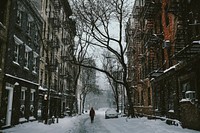 A person walking down the snow covered street surrounded by houses and trees in the city. Original public domain image from Wikimedia Commons