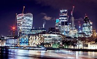 A cityscape background featuring well lit buildings and skyscrapers at night in London. Original public domain image from Wikimedia Commons