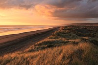 A cloudy sunset over the grassy sand dunes and coastal water at Port Waikato, Tuakau, Auckland, New Zealand. Original public domain image from Wikimedia Commons