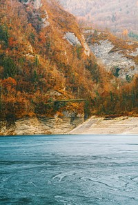 Mountains covered with orange-leafed trees near a frozen lake. Original public domain image from Wikimedia Commons