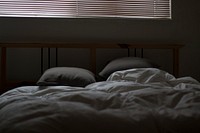 Ruffled gray covers and sheets with two pillows and a large window with blinds above it. Original public domain image from Wikimedia Commons