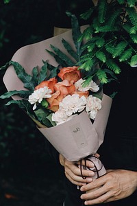 A person holding bouquet of white carnations and pink roses wrapped in decorative paper. Original public domain image from Wikimedia Commons