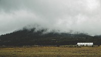 A white building on a field near a fog-shrouded hill. Original public domain image from <a href="https://commons.wikimedia.org/wiki/File:Field_by_a_misty_hill_(Unsplash).jpg" target="_blank" rel="noopener noreferrer nofollow">Wikimedia Commons</a>