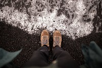 First person view of boots on the black sand by the foamy ocean in Iceland. Original public domain image from Wikimedia Commons