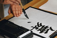 A close-up of a person practicing brush calligraphy.. Original public domain image from <a href="https://commons.wikimedia.org/wiki/File:Kanji_(Unsplash).jpg" target="_blank" rel="noopener noreferrer nofollow">Wikimedia Commons</a>