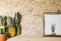 A group of pineapples next to a cactus plant and picture frame.. Original public domain image from Wikimedia Commons