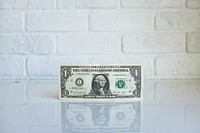 A one dollar bill leaning against the wall on a glossy surface. Original public domain image from Wikimedia Commons