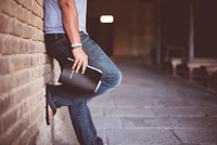 Man holding holy bible leaning on bricked wall. Original public domain image from <a href="https://commons.wikimedia.org/wiki/File:Ben_White_2016-11-11_(Unsplash).jpg" target="_blank">Wikimedia Commons</a>