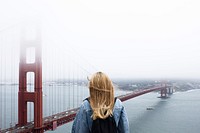 A blonde woman with a backpack looking at the Golden Gate Bridge. Original public domain image from <a href="https://commons.wikimedia.org/wiki/File:Sightseeing_Alone_(Unsplash).jpg" target="_blank" rel="noopener noreferrer nofollow">Wikimedia Commons</a>