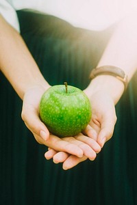 Woman wearing watch and green dress, holding green apple with sunlight streaming in. Original public domain image from Wikimedia Commons