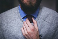 A bearded man in a blue shirt and gray sweater adjusting his tie. Original public domain image from Wikimedia Commons