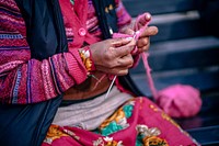 A person wearing a lot of pink clothing knitting with pink yarn in Manali. Original public domain image from <a href="https://commons.wikimedia.org/wiki/File:Weaving_a_Scarf_(Unsplash).jpg" target="_blank" rel="noopener noreferrer nofollow">Wikimedia Commons</a>