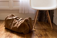 A leather duffel bag on the floor next to a small white chair. Original public domain image from Wikimedia Commons