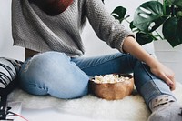 Woman in a cropped gray sweater sits on a furry rug with a bowl of popcorn. Original public domain image from Wikimedia Commons