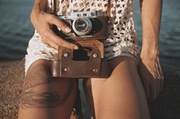 Woman holding a vintage camera and sitting by the water. Original public domain image from Wikimedia Commons