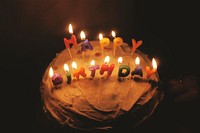 A birthday cake with frosting and happy birthday candles burning in a dark room. Original public domain image from <a href="https://commons.wikimedia.org/wiki/File:Happy_birthday_candles_(Unsplash).jpg" target="_blank" rel="noopener noreferrer nofollow">Wikimedia Commons</a>
