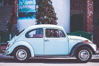 Retro blue Beetle parked on street in front of Christmas tree and blue poster. Original public domain image from Wikimedia Commons
