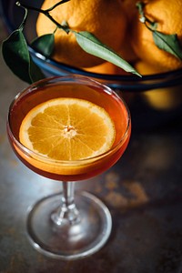 Macro view of a cocktail orange drink with a bowl of oranges with leaves by its side. Original public domain image from Wikimedia Commons