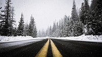 A blacktop road in a forest during snowfall; yellow traffic lines are painted crisply in the center. Original public domain image from Wikimedia Commons