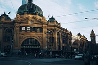 Cars on driving on road in front of Flinders Street Railway Station on clear day. Original public domain image from Wikimedia Commons
