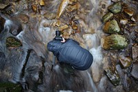 A photographer planting a tripod on a rocky bed of a creek. Original public domain image from Wikimedia Commons