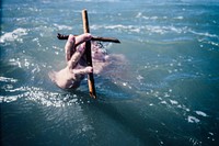 Man holding cross in water. Original public domain image from <a href="https://commons.wikimedia.org/wiki/File:Omaha_Beach,_Auckland,_New_Zealand_(Unsplash).jpg" target="_blank">Wikimedia Commons</a>