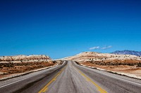 A desert road that goes to the horizon on a day with blue skies. Original public domain image from Wikimedia Commons