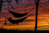 The silhouettes of two people in hammocks against a deep red and orange sunset in Neilston Pad. Original public domain image from Wikimedia Commons