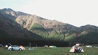 Campground with tents and cars in front of a forested mountain. Original public domain image from Wikimedia Commons