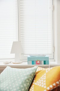 Colorful cushions near a TV remote and a colorful box on a windowsill. Original public domain image from <a href="https://commons.wikimedia.org/wiki/File:Cozy_bed_by_a_windowsill_(Unsplash).jpg" target="_blank" rel="noopener noreferrer nofollow">Wikimedia Commons</a>