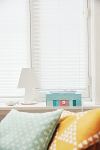 Colorful cushions near a TV remote and a colorful box on a windowsill. Original public domain image from Wikimedia Commons