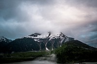 A tall mountain by a lake with its peak shrouded by dense clouds. Original public domain image from Wikimedia Commons