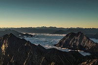Craggy mountains rising up above clouds during sunrise. Original public domain image from Wikimedia Commons