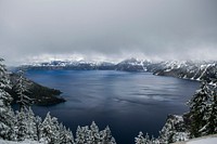 Crater Lake with a frozen shoreline of trees under thick gray fog and clouds. Original public domain image from Wikimedia Commons