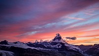 The sun setting over the snow capped Matterhorn mountain, with a blue and orange skyline. Original public domain image from Wikimedia Commons