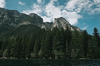 A forest-surrounded lake at the foot of a craggy mountain range. Original public domain image from <a href="https://commons.wikimedia.org/wiki/File:Mountaintops_over_the_lake_(Unsplash).jpg" target="_blank" rel="noopener noreferrer nofollow">Wikimedia Commons</a>